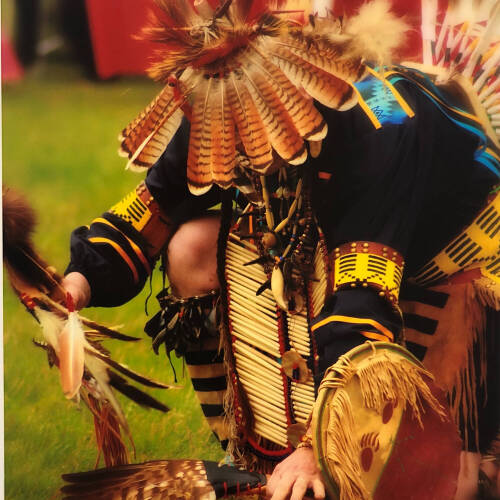 Color photograph of an indigenous person kneeling on the ground.